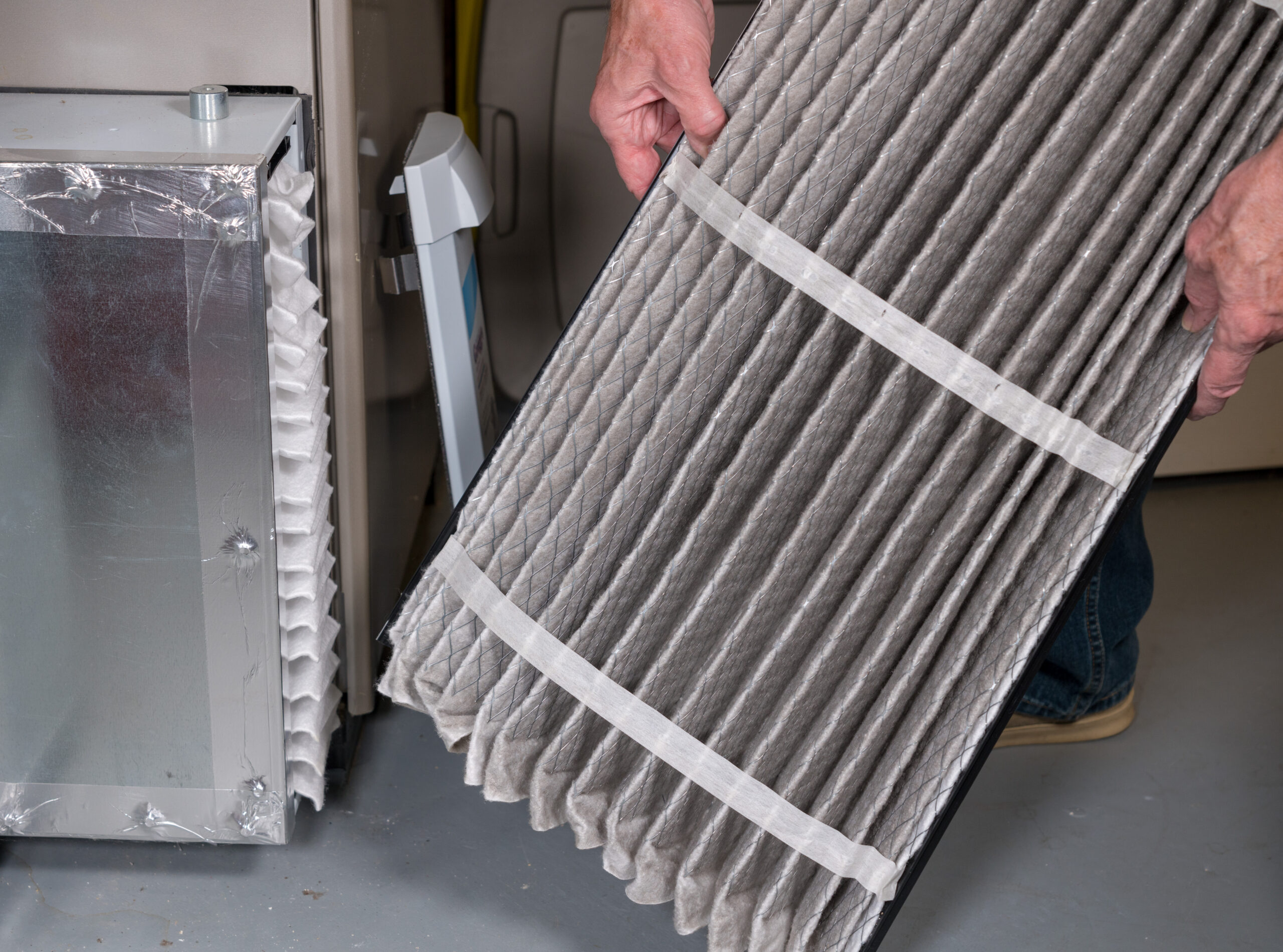 Senior caucasian man examining a folded dirty air filter in the HVAC furnace system in basement of home